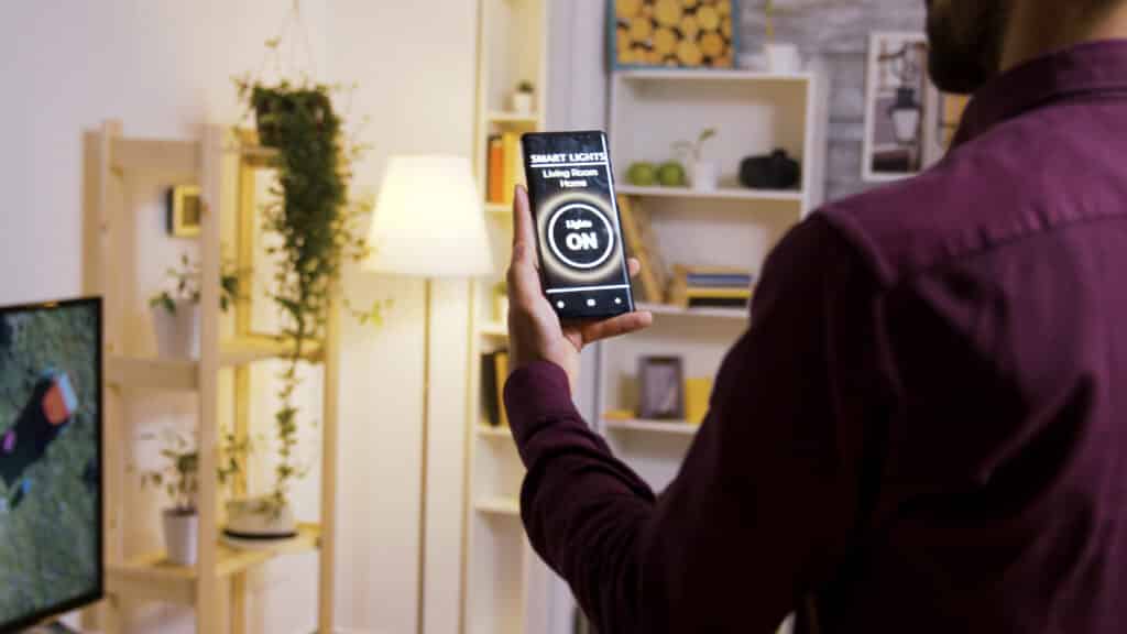 Person hält ein Smartphone in der Hand und steuert die Beleuchtung im Wohnzimmer über eine App.