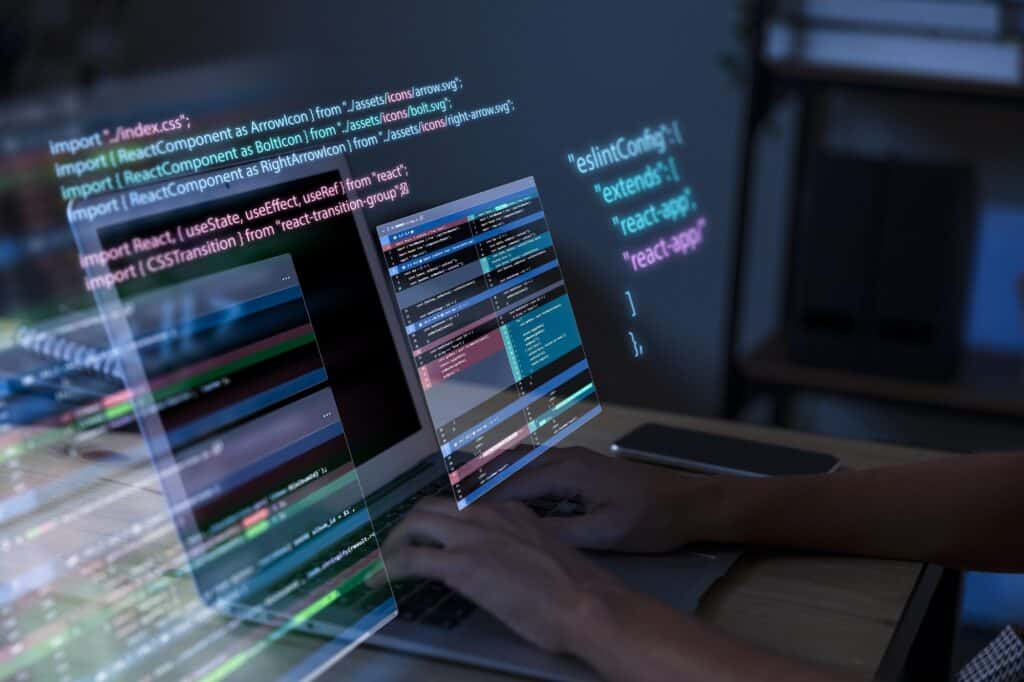 Eine Person tippt auf ihrem Laptop, aus dem verschiedene Code Zeilen hervorstehen.